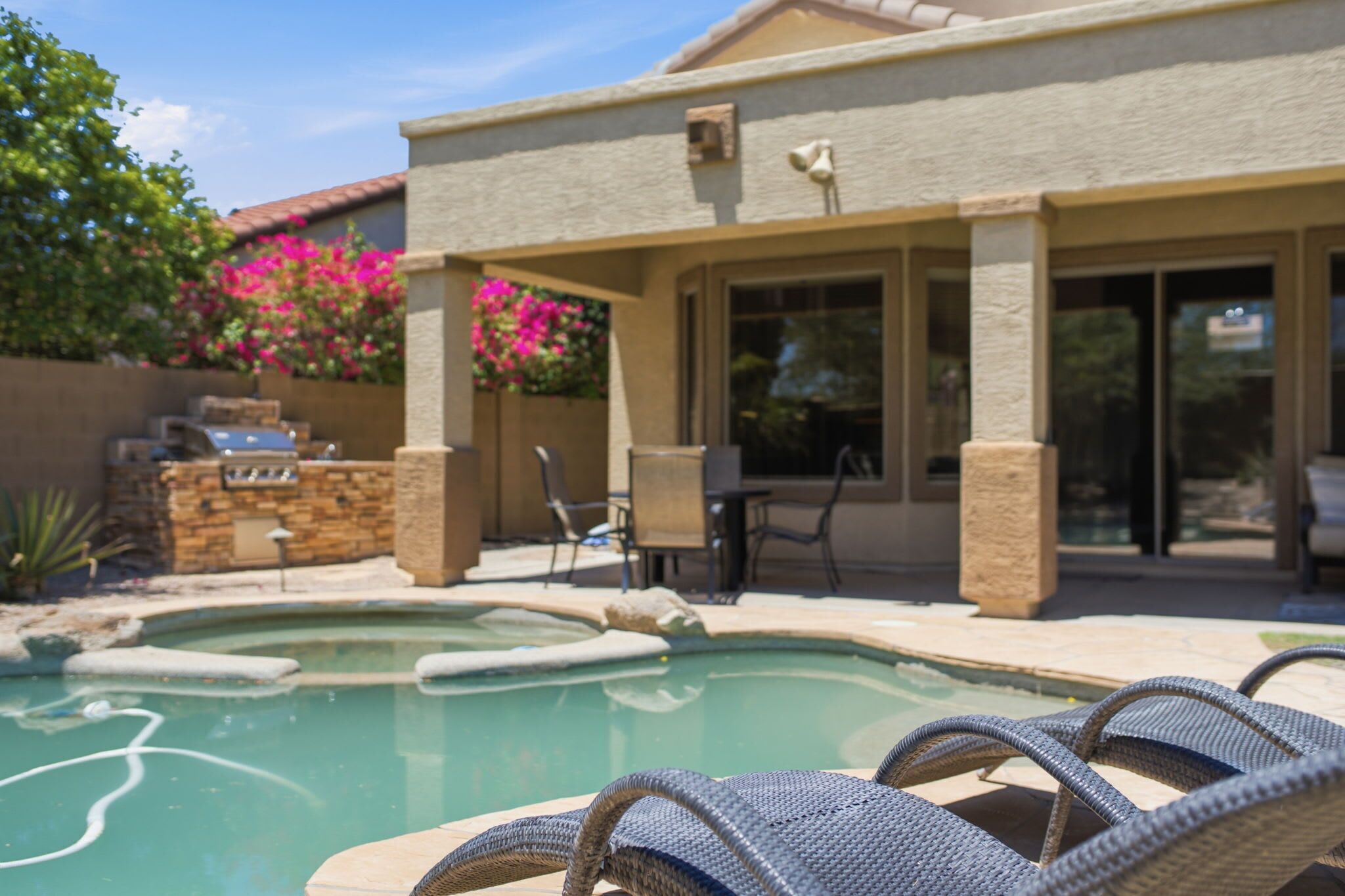 A pool area with lounge chairs, a barbecue grill, and a covered patio with chairs and a table.