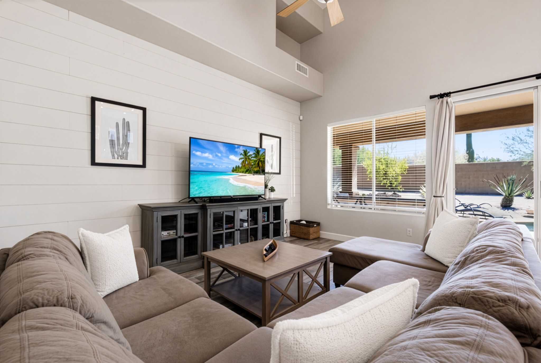 A living room with a flat-screen TV, a sofa, a coffee table, and a window with blinds.