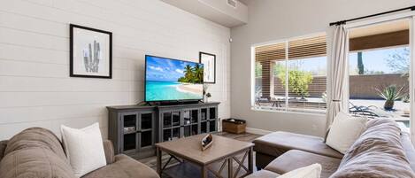 A living room with a flat-screen TV, a sofa, a coffee table, and a window with blinds.