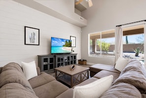 Ein Wohnzimmer mit Flachbildfernseher, einer Couch, einem Couchtisch und einem Fenster mit Jalousien.