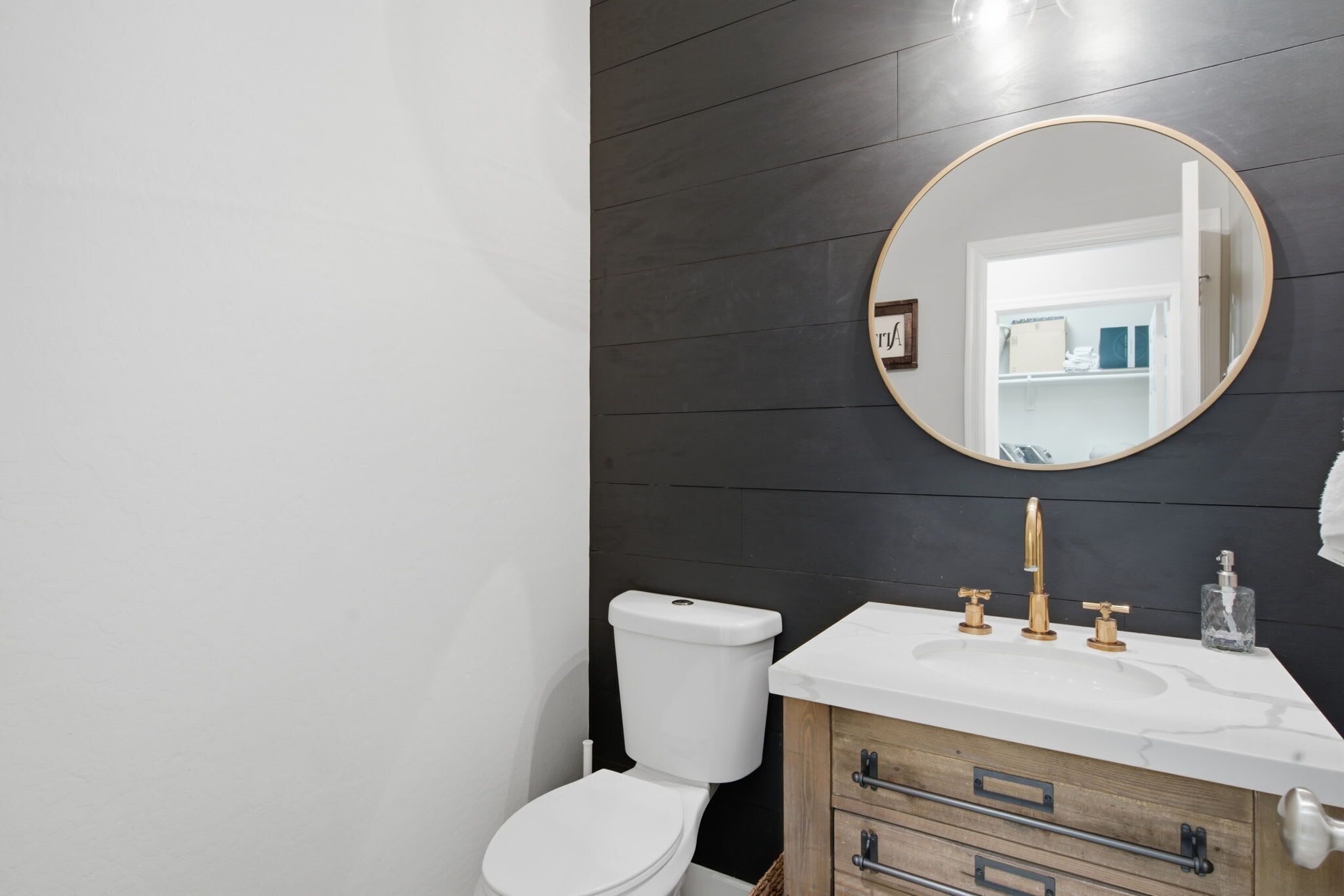 A bathroom with a white toilet, a vanity with a mirror, and a dark wooden wall.