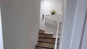 Una scala con gradini in legno e ringhiere bianche che porta a un pianerottolo con una porta e una piccola pianta.