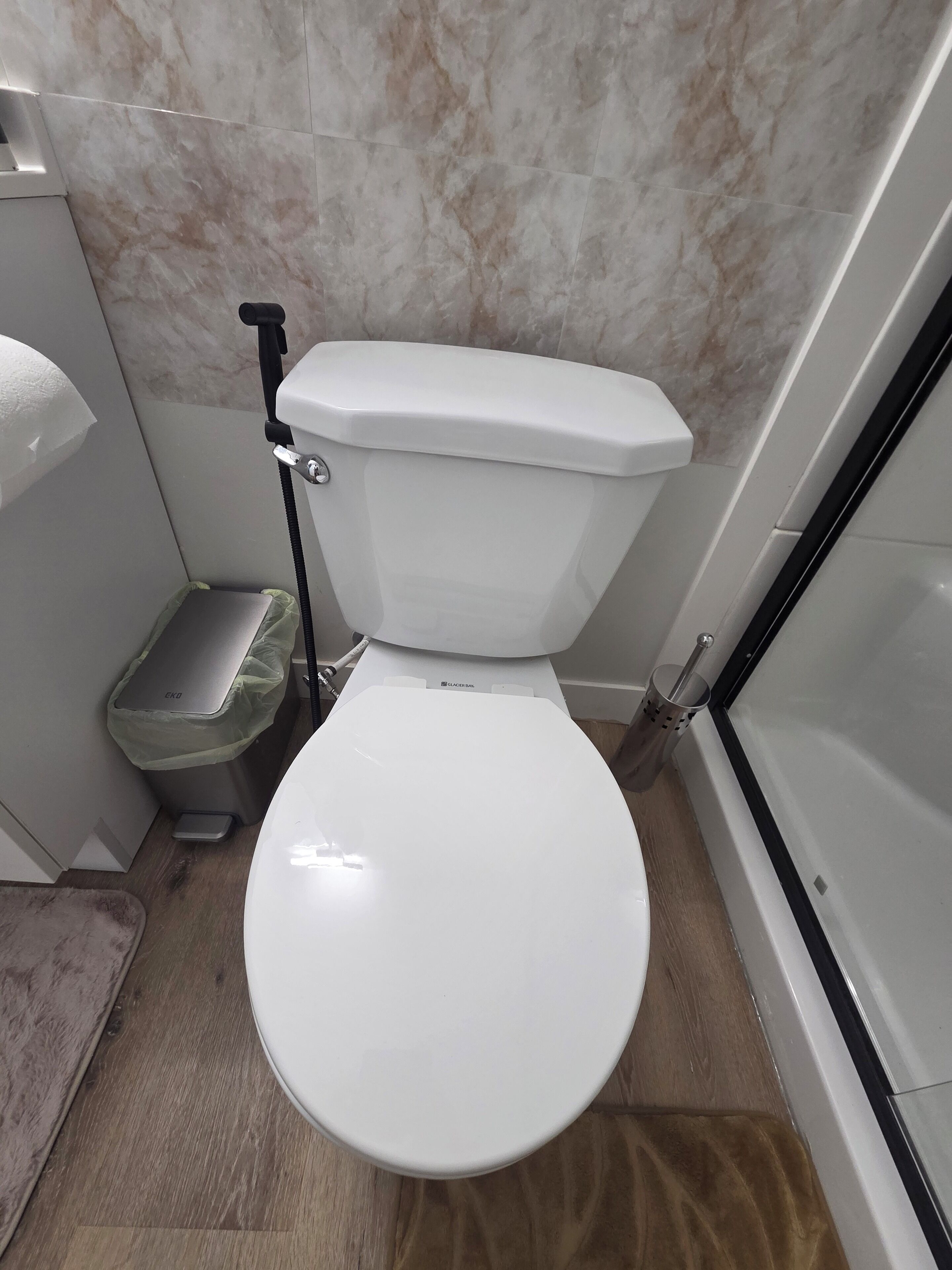 Een badkamer met een wit toilet, een kleine prullenbak en een douchehoek.