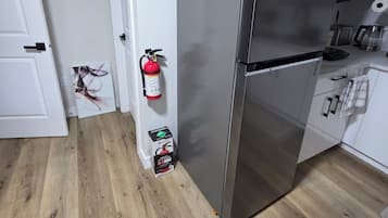 Une cuisine équipée d’un réfrigérateur en acier inoxydable, d’un plancher en bois, de meubles blancs et d’un extincteur fixé au mur.