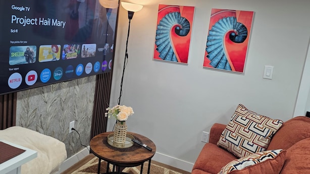 Un soggiorno con una TV a schermo piatto che mostra un film, un divano, un tavolino da caffè con un vaso e due opere d'arte astratte appese alle pareti.