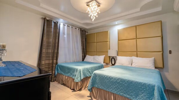 A hotel room with two beds, a desk, a chandelier, and a window with curtains. - Fantastic 6-bedroom resort with AC in sunny San Salvador, Luxury house villa (San Salvador)