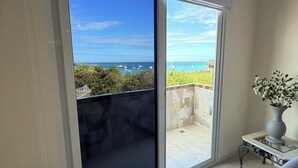 A room with a large sliding glass door leading to a balcony with a view of the sea and boats. - Katarma Deluxe Apartments (Puerto Baquerizo Moreno)