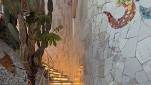 A staircase with illuminated steps leading upwards, surrounded by a mosaic wall and a cactus plant. - Katarma Deluxe Apartments (Puerto Baquerizo Moreno)