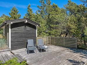 A wooden deck with two lounge chairs and a small shed.