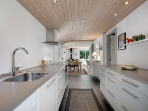Een moderne keuken met een centraal eiland, roestvrijstalen apparatuur en een houten plafond.