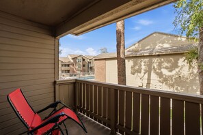 A balcony with a red chair, a view of neighboring buildings, and a clear sky. - Fully furnished, 1-bedroom condo in the heart of Tempe. (Tempe)