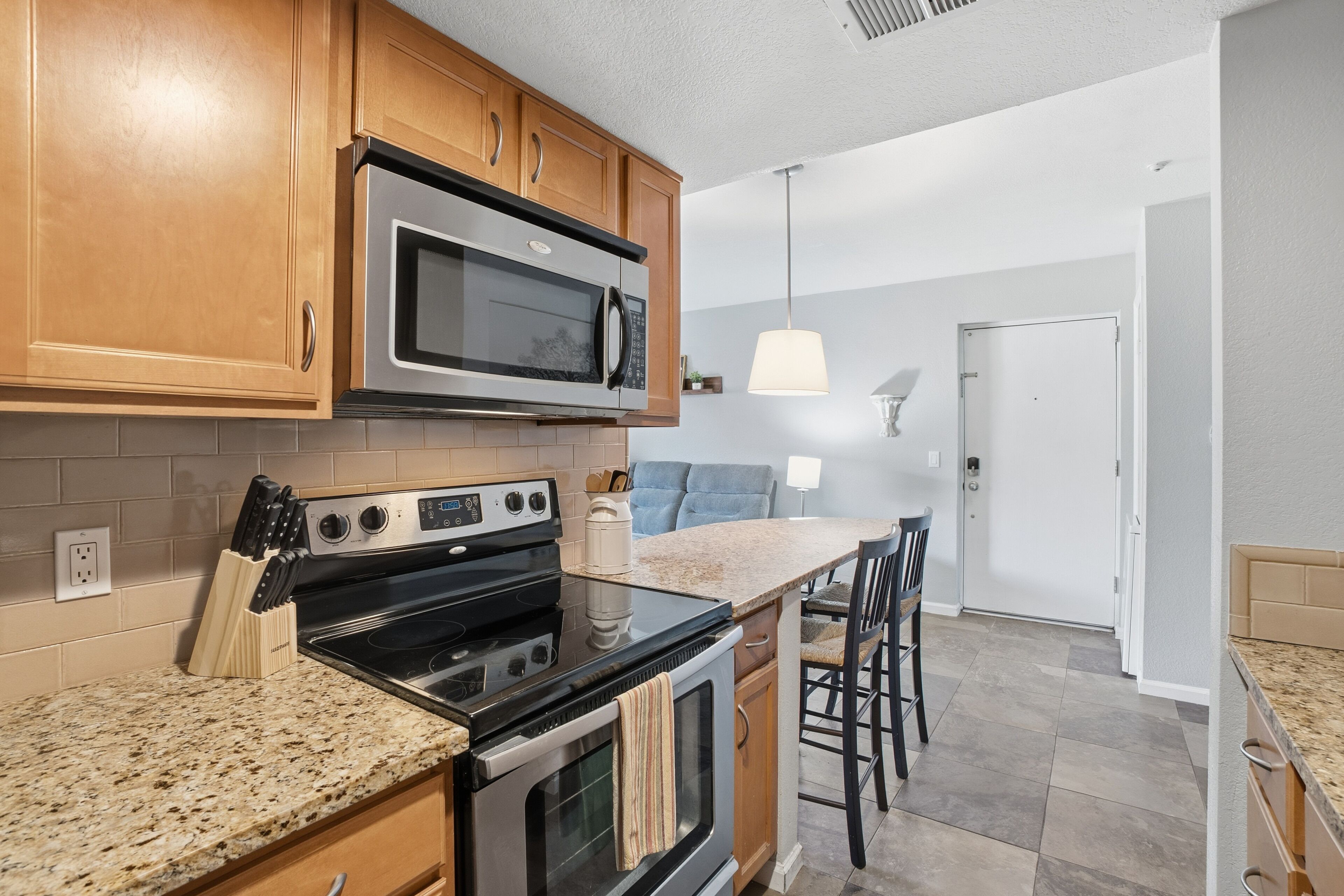 A kitchen with wooden cabinets, a stainless steel microwave, a stove, and a granite countertop.