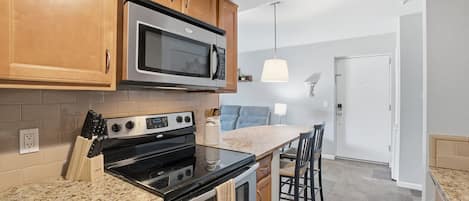 A kitchen with wooden cabinets, a stainless steel microwave, a stove, and a granite countertop.