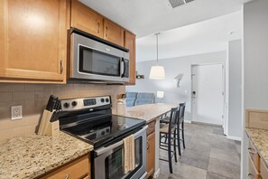 A kitchen with wooden cabinets, a stainless steel microwave, a stove, and a granite countertop. - Fully furnished, 1-bedroom condo in the heart of Tempe. (Tempe)