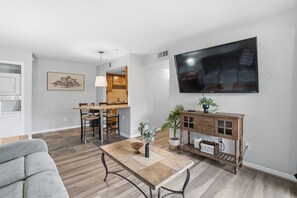 A modern living room with a flat-screen TV, a dining area with a wooden table and chairs, and a kitchen in the background. - Fully furnished, 1-bedroom condo in the heart of Tempe. (Tempe)