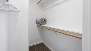 Ein kleiner, weiß getünchter Schrank mit einer Holzablage, einer Kleiderstange und einem zusammengerollten Handtuch.