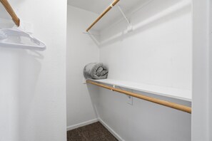 A small, white-walled closet with a wooden shelf, a hanging rack, and a rolled-up towel. - Fully furnished, 1-bedroom condo in the heart of Tempe. (Tempe)