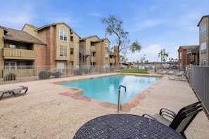 A swimming pool with a metal ladder, surrounded by a fence. There are lounge chairs and a table. - Fully furnished, 1-bedroom condo in the heart of Tempe. (Tempe)
