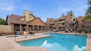 Ein Swimmingpool mit Liegestühlen und Grillplatz, umgeben von Backsteingebäuden mit Balkonen.