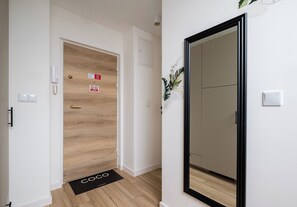 A hallway with a wooden door, a black-framed mirror, and a doormat. - Rondo ONZ Signature Studio (Warszawa)