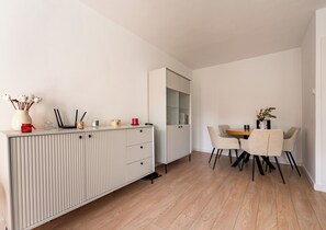 Eine moderne Küche mit weißen Schränken, einem Esstisch mit Stühlen und einem kleinen Beistelltisch mit Dekoration.