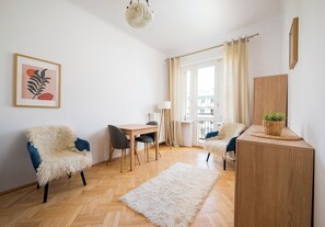Ein modernes Wohnzimmer mit Holzdielen im Fischgrätmuster, einem weißen, flauschigen Teppich, einem Schreibtisch mit Stuhl und einem Sofa mit blauen Kissen.