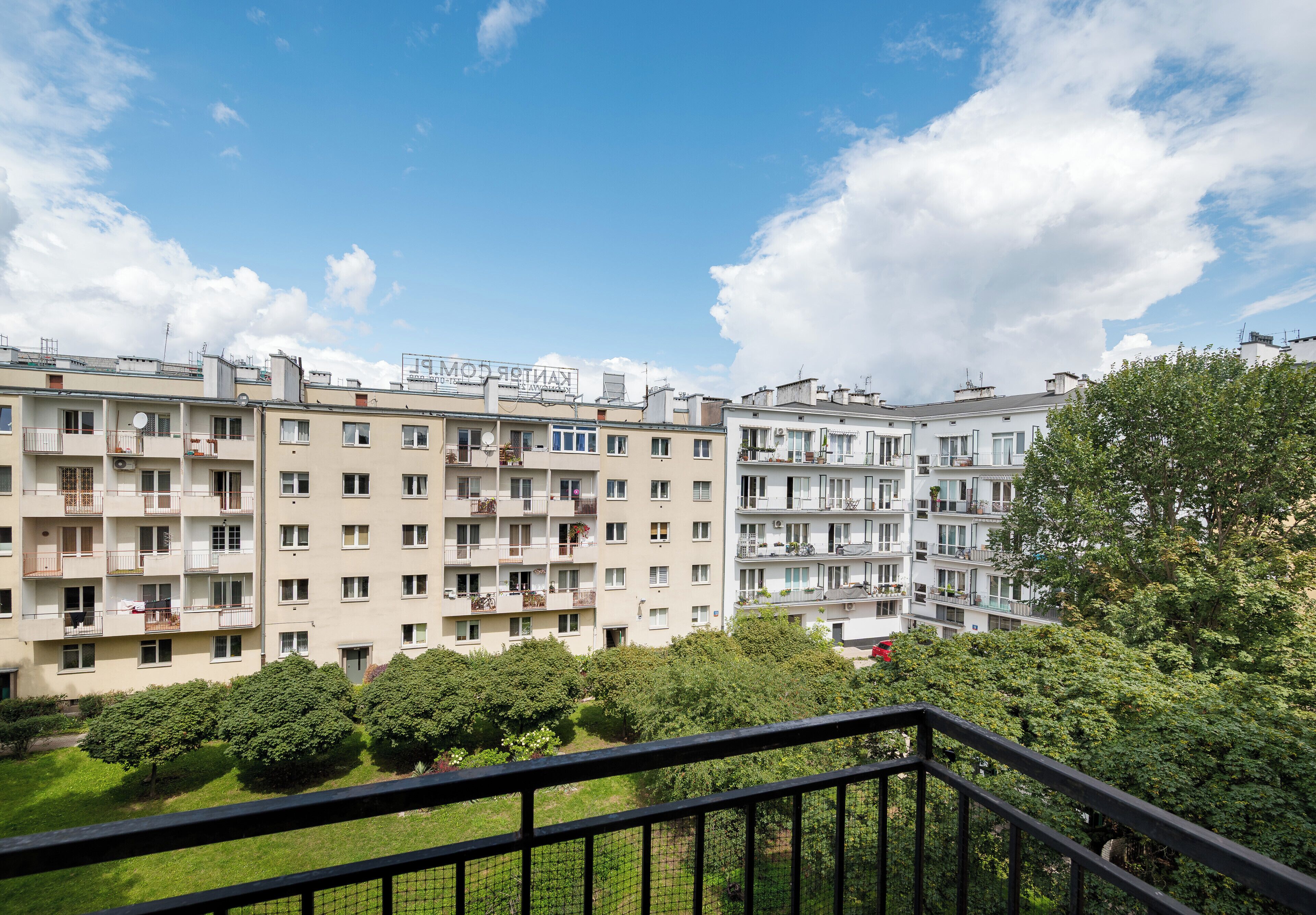 A multi-story residential building with balconies, a clear sky, and surrounding greenery.