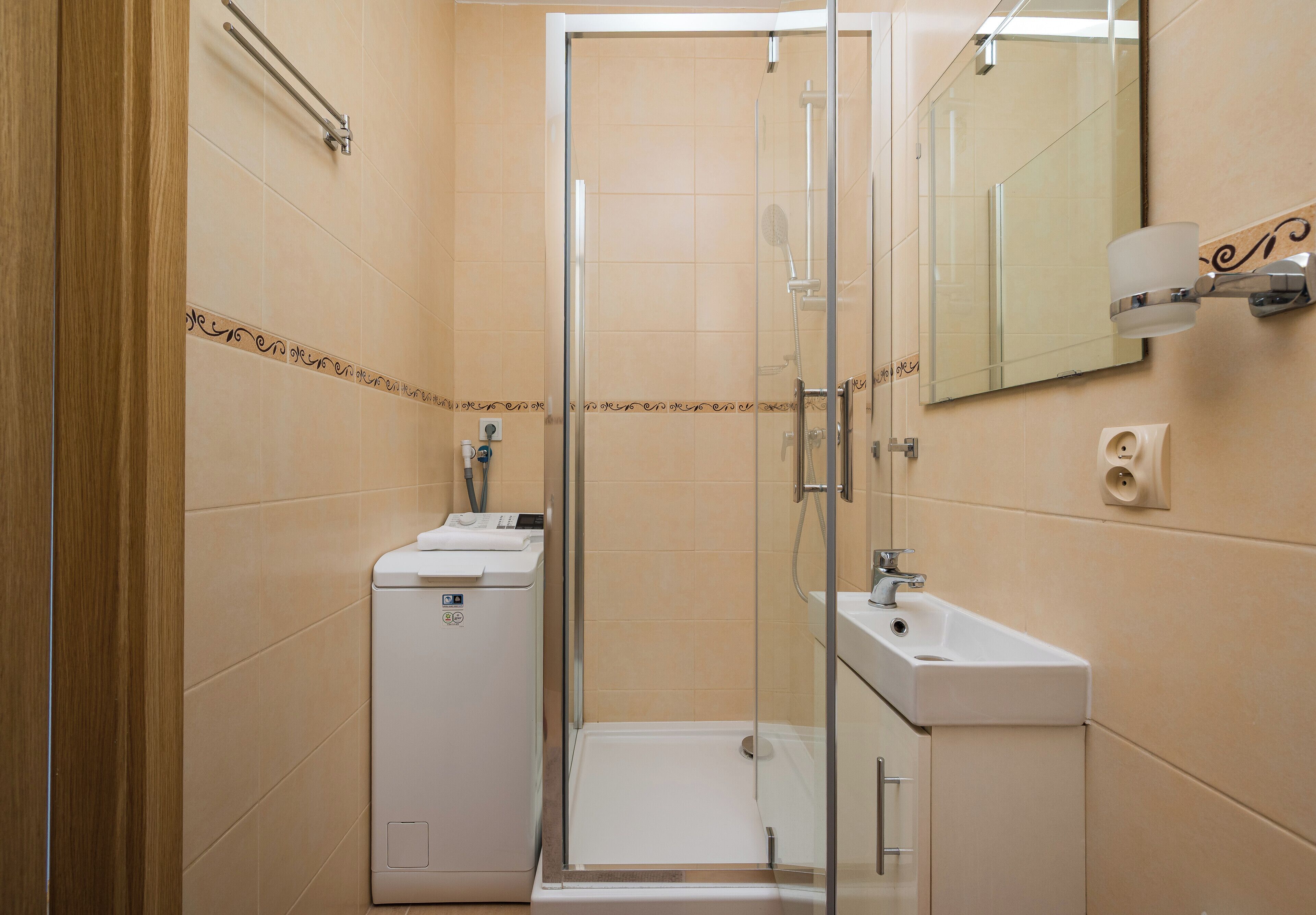 A bathroom with a glass shower enclosure, a sink, and a washing machine.