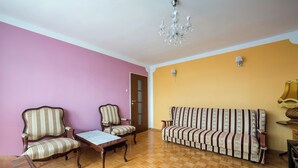 Une pièce dotée d’un parquet en bois, de deux fauteuils rembourrés, d’un canapé, d’une table, d’un lustre et d’une porte.