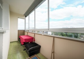 A balcony with a table and a sofa, large windows, and a view of buildings and trees. - Metro Targówek Heritage Apartment (Warszawa)
