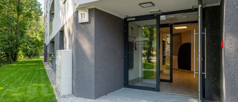 A modern building entrance with a glass door, a visible number '11' sign, and a paved pathway leading to the entrance.