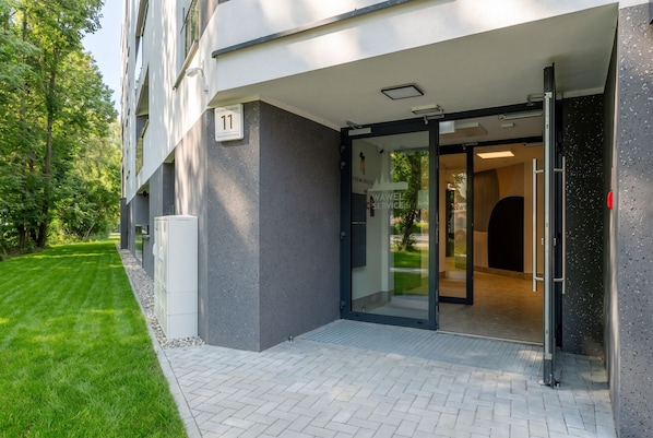 Une entrée moderne avec une porte en verre, un panneau indiquant clairement le numéro « 11 », et un chemin pavé menant à l’entrée.
