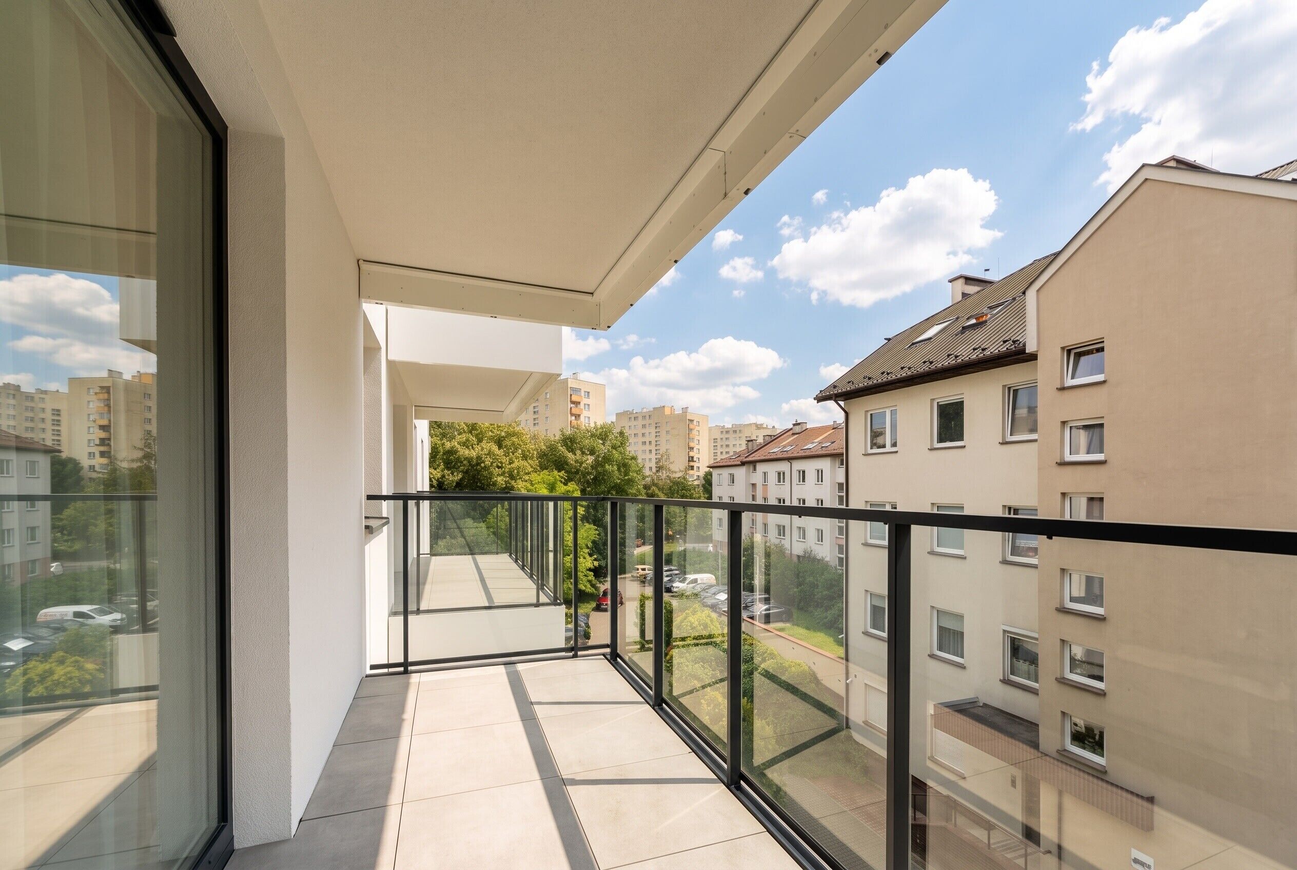 Een balkon met glazen balustrade, met uitzicht op een woongebied met meerdere gebouwen.