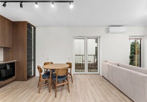 A modern kitchen with built-in appliances, a dining area with a round table and chairs, and a living area with a sofa and a sliding glass door leading to an outdoor space. - Rondo Matecznego Prestige Apartment (Kraków)