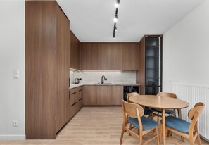 A modern kitchen with wooden cabinets, a built-in oven, and a dining area with a round table and chairs. - Rondo Matecznego Prestige Apartment (Kraków)