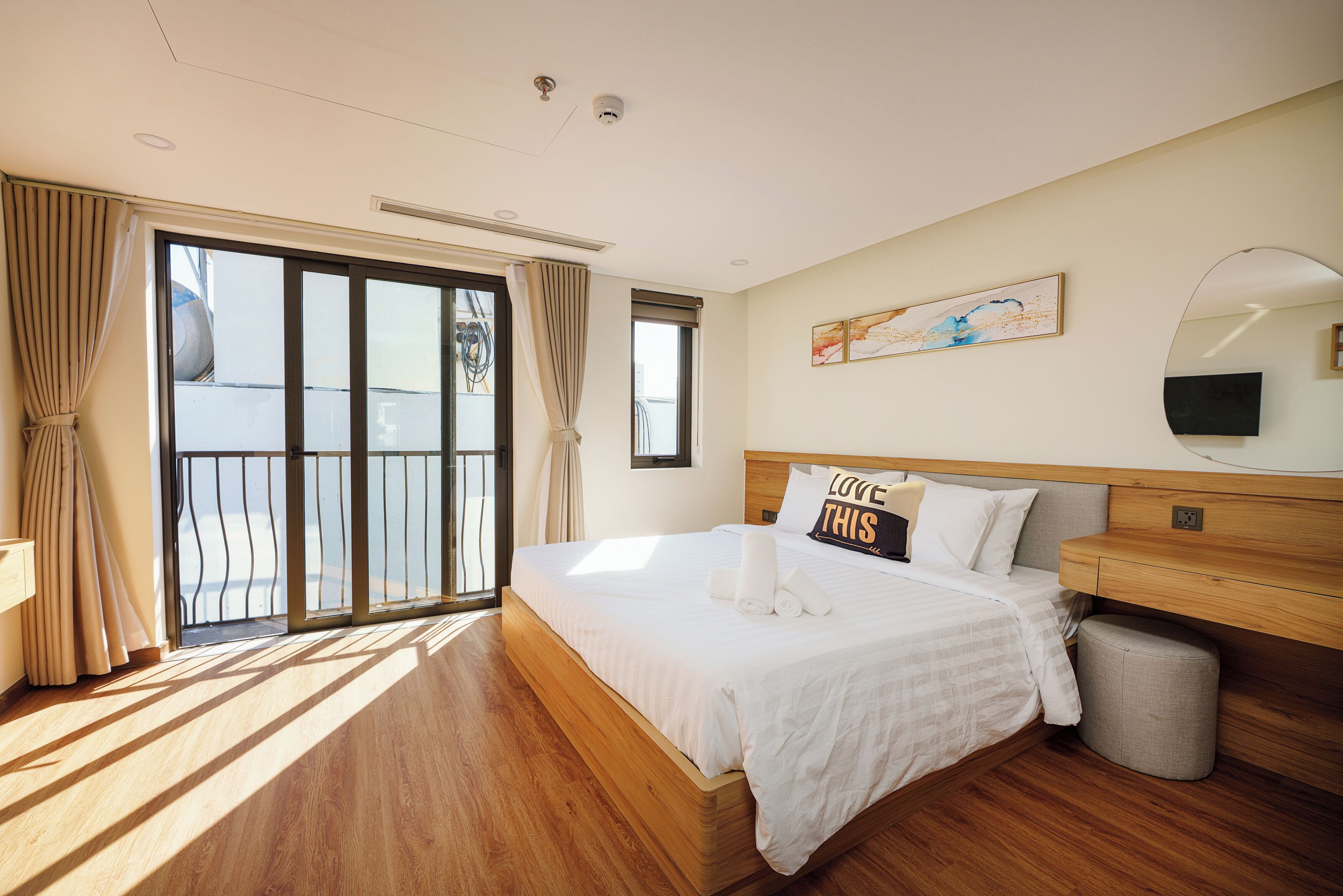 A hotel room with a large bed, a wooden headboard, a bedside table, a mirror, and a view through a sliding glass door.
