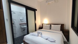 A hotel room with a bed, a bedside table, a nightstand, a mirror, a bathroom with a sink, and a shower. - Moonrise Rooms (Pecatu)