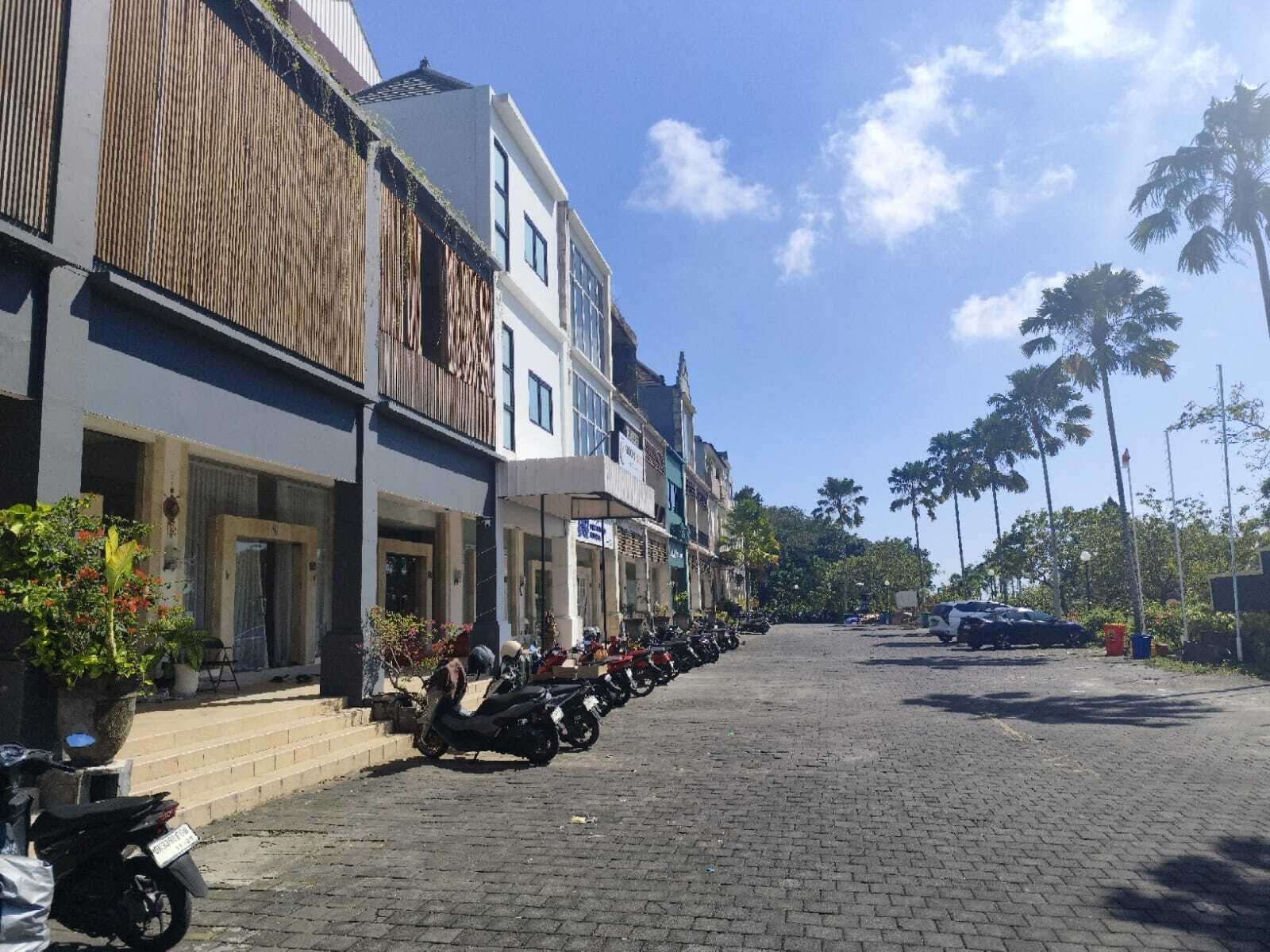 Eine Straße gesäumt von Gebäuden, eine Reihe geparkter Motorräder und Palmen im Hintergrund.