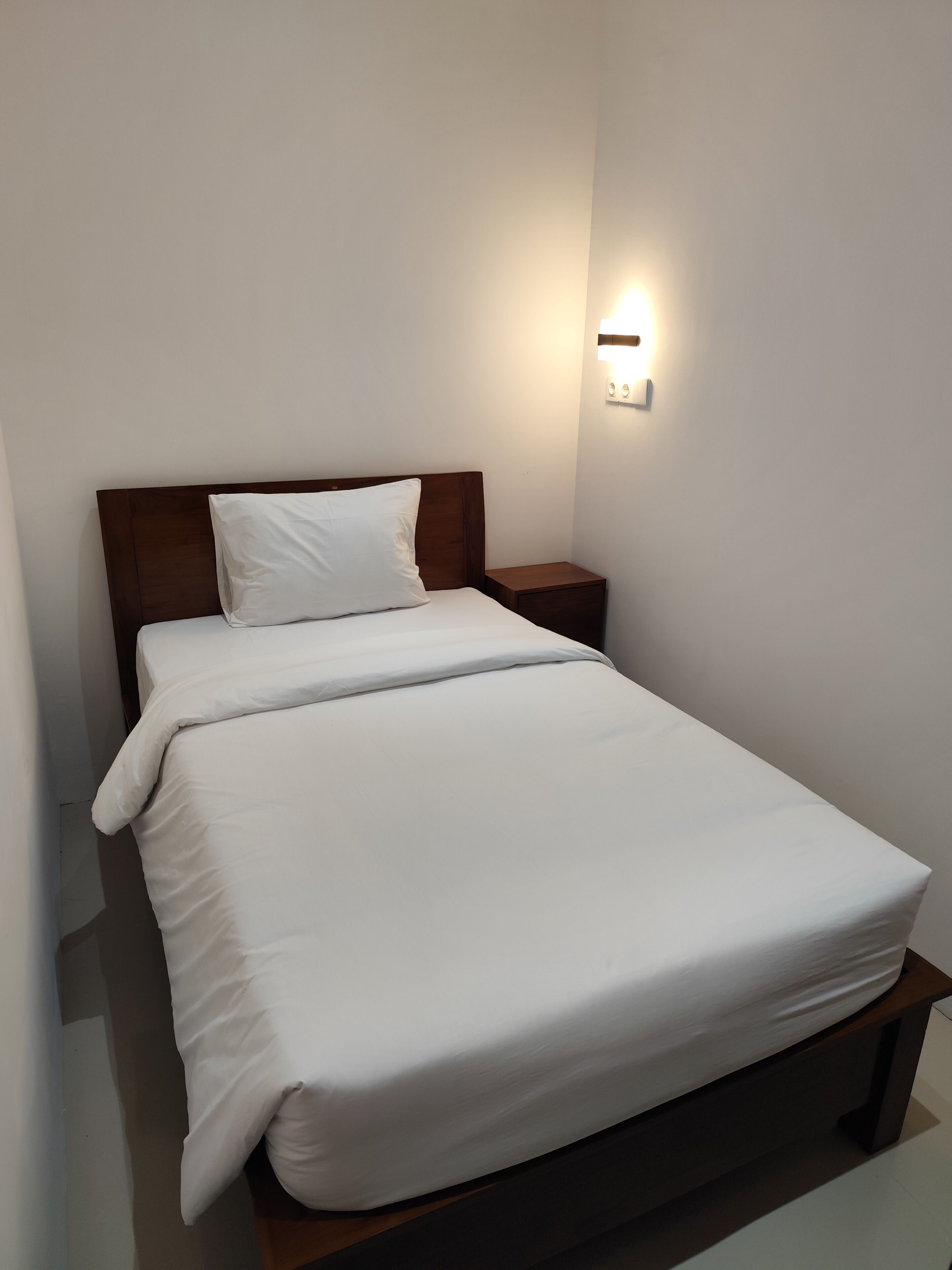 A single bed with a wooden headboard, a bedside table, and a wall-mounted light fixture.