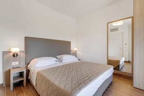 Ein Hotelzimmer mit Bett, Nachttischen, einem Spiegel und einer Tür.