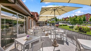 An outdoor patio with tables and chairs, large umbrellas, and a view of the street and buildings.