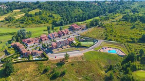 An aerial view of a residential area with houses, a swimming pool, and green fields.