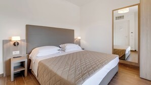 A hotel room with a bed, bedside tables, a nightstand, a mirror, and a door.