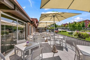 Eine Außenpatio mit Tischen, Stühlen und großen Sonnenschirmen, mit Blick auf die Straße und die Gebäude.