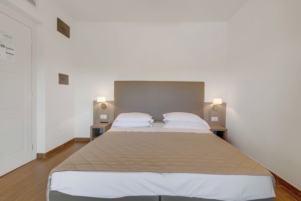 A hotel room with a large bed, two bedside tables, and wall-mounted lamps.