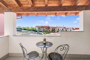 Ein Balkon mit Tisch und zwei Stühlen, mit Blick auf eine Wohngegend mit Häusern und einer Straße.