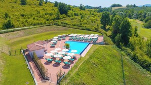 Una piscina con tumbonas y sombrillas, rodeada de jardines y vistas al campo.