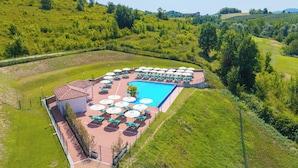 Una piscina con lettini e ombrelloni, circondata da un'area verde con vista sulla campagna.