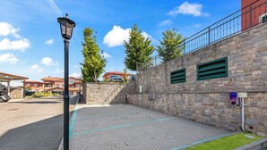 Un'area esterna pavimentata con un muro in pietra, un lampione e un cordolo verde.