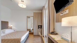 Una camera d'albergo con un letto, un comodino, una lampada, una TV e una scrivania con il telefono.